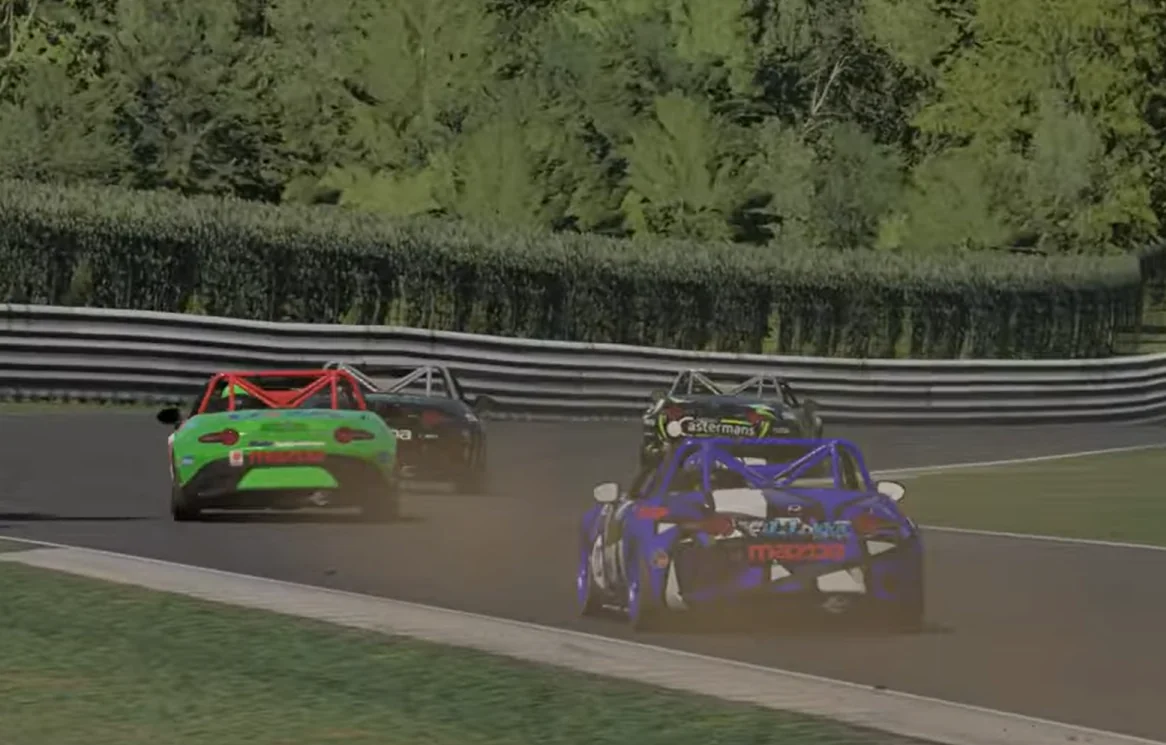 Pack Jostle at Corner Exit - A close-up, rear-facing view of a green race car leading a blue and black car as a tight pack of sports cars exits a tight corner on the racetrack