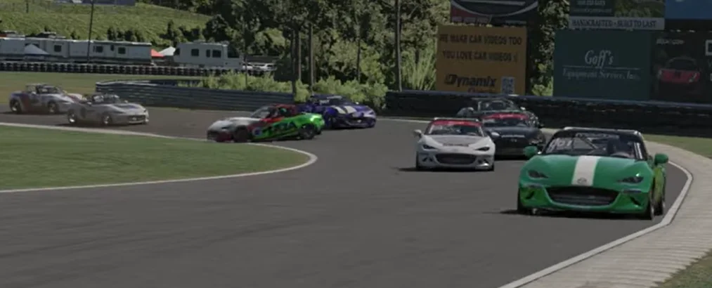 Sweeping Curve Racing - An elevated view of multiple Mazda MX-5 race cars navigating a sweeping, banked left-hand turn on an asphalt track, with trees and roadside advertising in the background
