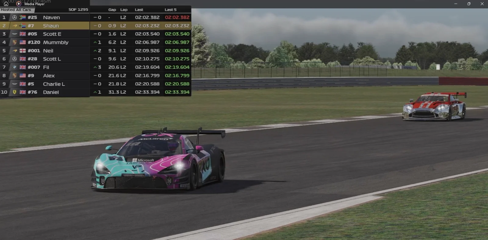 Pink teal McLaren GT3 leading silver red Aston Martin Vantage GT3 on Lap 2 with headlights illuminated